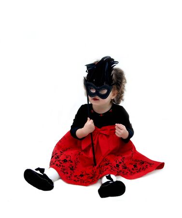 Baby plays with mask for Mardi Gras Parade   She is wearing a bright red dress and holding a black mask with black feathers の写真素材