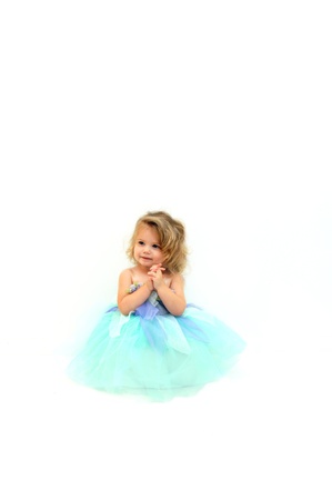 Beautiful little girl pretends to be a ballerina.  She is wearing a mint colored tutu and is clasping her hands in delight.  Blond curls spring freely around her face.の写真素材