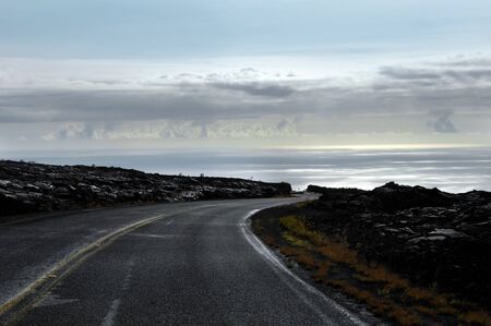 Daybreaks along the road through Hawaii Volcanoes National Park on the Big Island   Curving, snaking road winds down toward the coastline   Lava field is lit in all its lumpty, bumpy landscape の写真素材