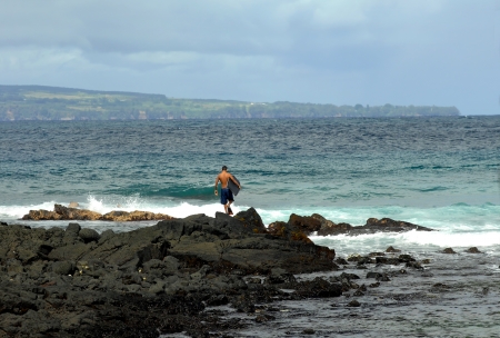 Young man carrying a boogie board and wearing flippers walks out across the rocks to enter the ocean for a day of fun boogie boarding の写真素材
