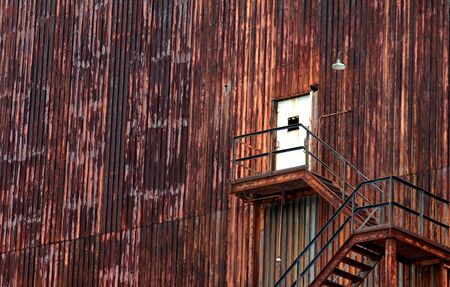 Background image of derelict industrial building.  Doorway has broken window and stairway and walls are peeling and completely rusted.の写真素材