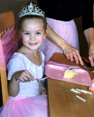 Beautiful little girl is enjoying her ballerina birthday party   She is wearing a crown and pink tutu   Her fork is poised ready to eat her slice of cake の写真素材