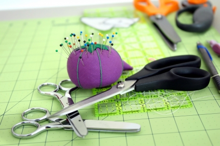 Sewing tools of the trade lay on a green cutting matt   Pins are stuck in purple pin cushion and three pair of different sized scissors lay in a stack on table top の写真素材