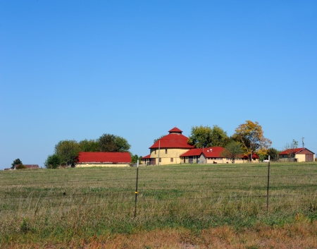 Round wooden barn has red shingled roof.  Home and outbuildings are constructed out of same materials.  Farm is located outside of Derby, Kansas.のeditorial素材
