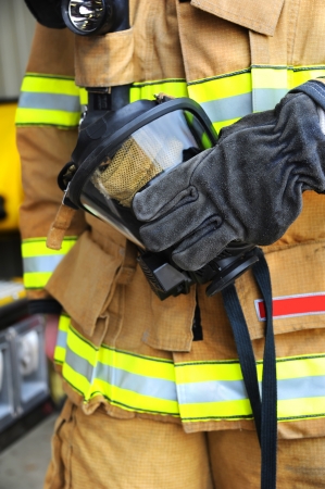 Fireman holds gas mask in his gloved hand.  Mask is black with straps and protective netting.の写真素材
