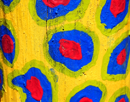 Bare trunk of tree is painted in yellow and decorated with red, blue and green circular blobs 