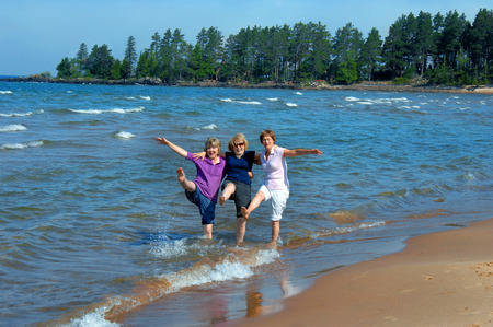 Three sisters revisit their childhood and kick and splash in the waters of Lake Superior in Upper Peninsula, Michigan.  They are laughing and kicking up their heels.の写真素材