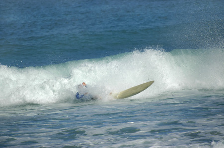 Surfer crashes and is buried in spray as he enjoys surfing the waters off the shore of Kauai,...