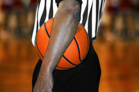 Referee, at high school basketball game, stands with his arm across the basketball.の写真素材
