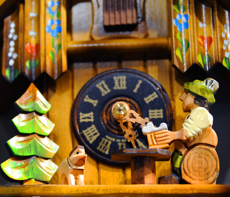 Cuckoo clock shows man sitting on a log drinking a bear while his dog keeps him company.  Swiss chalet and clock piece in background.の写真素材