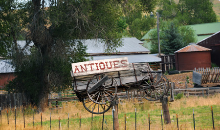 Dilapidated and weathered, wooden wagon hangs as part of an antique sign advertising antiques for sale.  Sign hangs in Montana.の写真素材