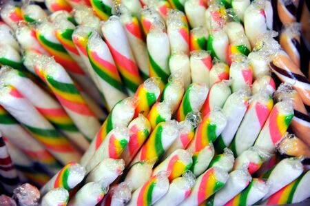 Bunch of striped, candy sticks sit ready for sale.  Stripes are orange, yellow and green.の写真素材
