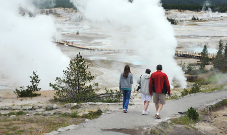 Family visits Norris Geyser Basin in Yellowstone National Park.  They carry cameras and a hiking down to geysers via walkway.のeditorial素材