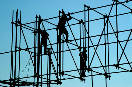 Morning sunlight silhouettes three construction workers as they balance on the pipes of a new construction in Mexico City, Mexico.の写真素材