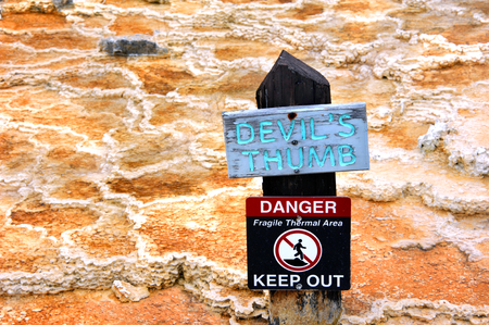 Sign identifies Devil's Thumb and also warns visitors to Yellowstone National Park of the danger of the thermal area.  Sign is wooden with aqua lettering.の写真素材