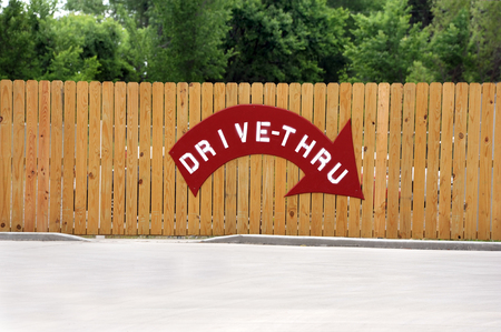 Business has painted a sign on back fence that points the way to the drive through.  Sign is painted on wooden fence and has a curved red arrow.の写真素材