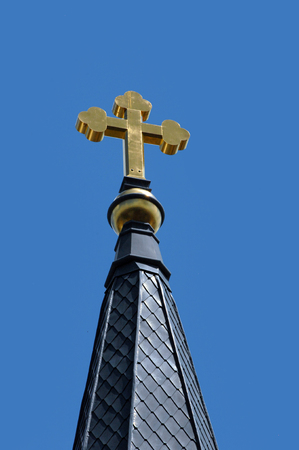 Gold cross glows gold in a sunny sky in Cullen, Alabama.  Cross tops one of the steeples of the Sacred Heart of Jesus Catholic Church.の写真素材