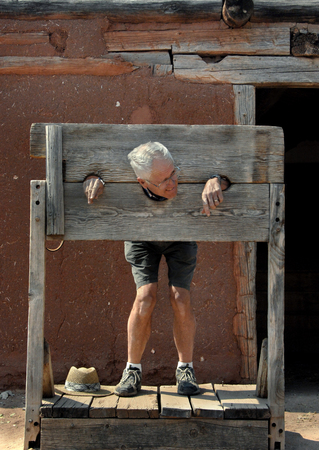 Tourist in stocks.  Senior male has his head through the wooden neck and hand holes of a wooden stock.  の写真素材