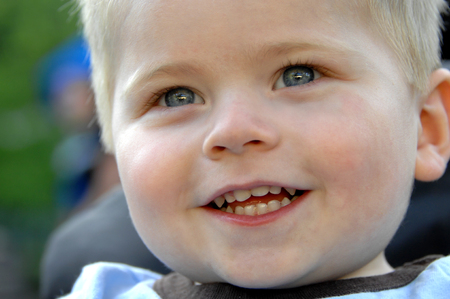 Sweet little innocent smile touches this baby's face.  He has on a light blue shirt and has blond...
