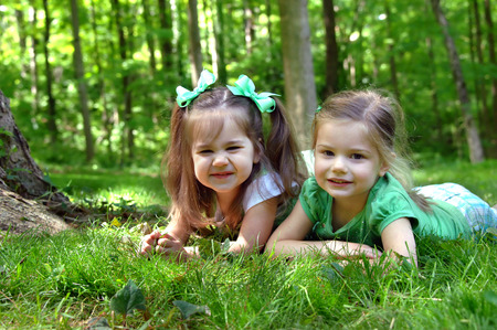 Two sisters lay on the grass of their yard.  Each sister has a different expression on their faces.  One sister looks impish and the other sweet and serene.の写真素材