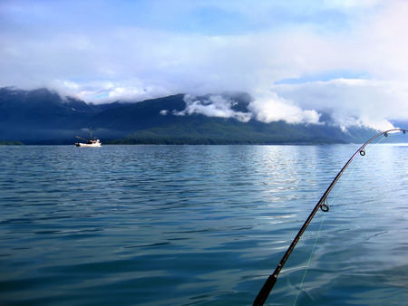 Beautiful Valdez Bay in the early morning provides peaceful fishing.  Clouds hang low over the Chugach Mountains, and a ship glides over the water.の写真素材