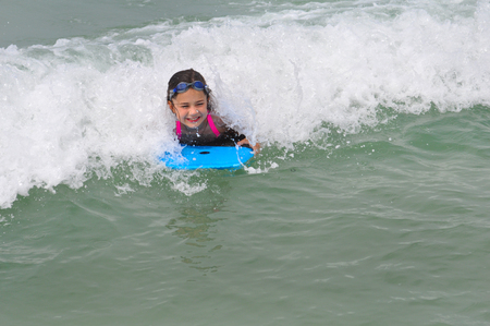Little girl exits a wave on her boogie board at Madeira Beach, Florida.  She is smiling and riding a blue board.の写真素材