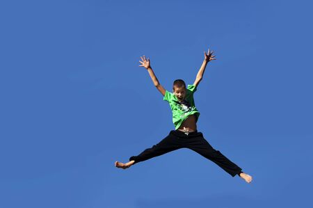 Young boy jumps for joy and propels himself into the air.  He embraces his feelings and flings his arms and legs wide.の写真素材