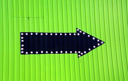 Neon green wall has black arrow pointing the way.  Arrow has white dots lining it.の写真素材