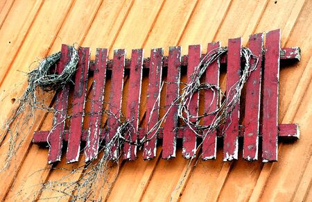 Abstract version of a rustic and weathered, red wooden fence hanging on a wooden wall.  Tattered rope decorates boards.の写真素材
