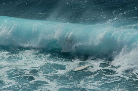 Surfer is swallowed by a large wave during a surfing competition.  His white surfboard floats free. ...