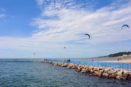 Vacation goers walk the causeway to the Holland Harbor Lighthouse.  They enjoy watching Kiteboarders on Lake Michigan.の写真素材