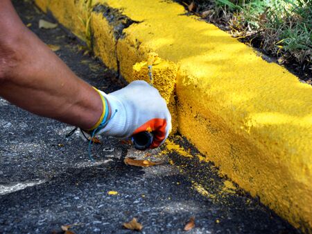 Street workers repaint the street curb in yellow.  They are using paint rollers.の写真素材