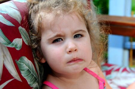 Little girl has her face screwed up in a scowl.  Her attitude is crabby and fussy.  She has curly...