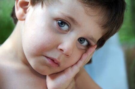 Close up of a little boy looks very sad.  He is leaning his head on his hand and looking at camera.の写真素材