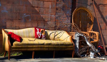 Outdoor living at its worst.  Sofa and chair are wet and faded.  They sit in a pile of junk in an alley.の写真素材