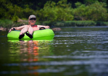 Mature woman easily rides, in her lime green intertube, down the gentle Caddo River in Glenwood, Arkansas.  She is alone on the river and enjoying her solitude.の写真素材