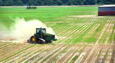 Farmer drives tractor over field discing it up.  Dust boils from back of tractor.