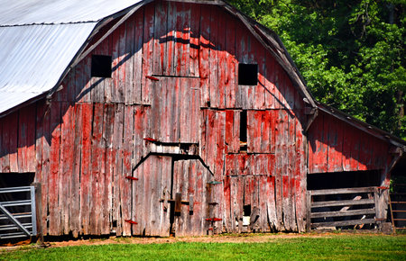 Closeup of the front of this old, red wooden barn, shows broken and missing boards.  Exterior has been exposed to the elements of time.の写真素材