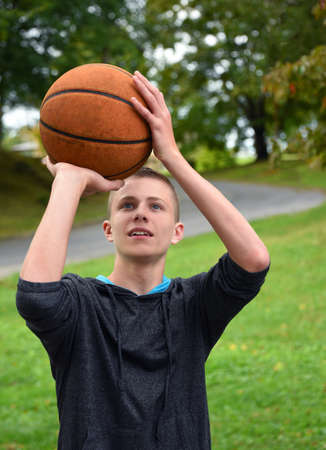 Young teen boy focuses on the goal.  He is practicing basketball in his backyard.  He is concentrating on making his shot.の写真素材
