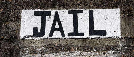 Old concrete and stone jail, is topped with a painted white and black sign that simply states Jail.