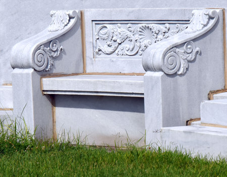 Solitary marble bench sits alone.  It is elegant with markble scrollwork and engraving.  Secluded spot calls for contemplation.の写真素材