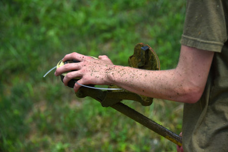 Young man struggles to restring weed eater.  His hand and arm is covered in grass from trimming...
