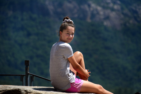 Young teenager, sits at the top of Chimney Rock and enjoys the sunshine and the view.  She has on pink shorts and grey tee shirt.の写真素材