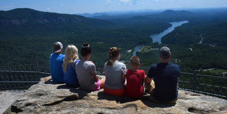 Family of six sit on edge of rock admiring the view from Chimney Rock, Chimney Rock State Park,...