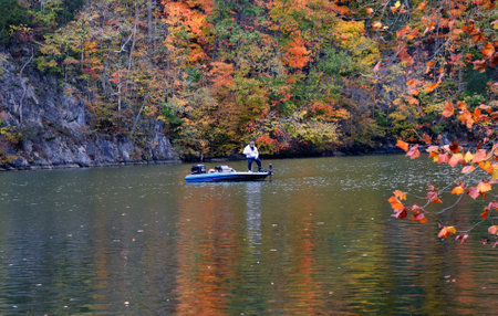 Fisherman wets a line on the calm waters of the Holston River in Warriors Path State Park in Kingsport, Tennessee.  Autumn has colored the trees.の写真素材