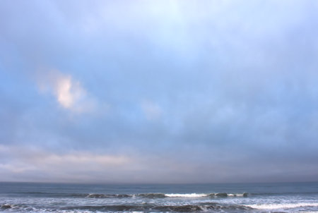Cloudy morning sky is lit by blues, purples and pinks as the sun rises on the Oregon Coast.  Gentle waves wash ashore.の写真素材