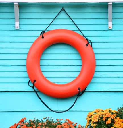 Orange life ring serves as part of landscaping decoration.  Ring is vibrant against turqoise home.