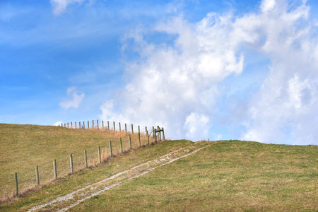 Dirt lane disappears into the clouds as it passes over a hilltop.  Rustic wooden fence also tops...