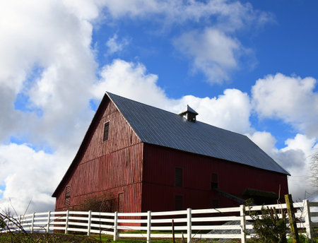 Red, wooden barn is well kept.  It has a tin roof and small cupola.  White wooden fence surrounds barn.の写真素材