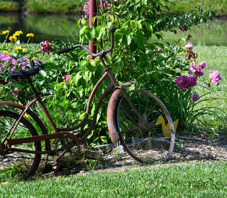 Vintage bicycle leans against a red pole as part of landscaping.  Summer flowers bloom around rusty bike.の写真素材